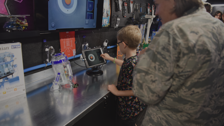 A woman in a military uniform behind a boy looking at a screen. 
